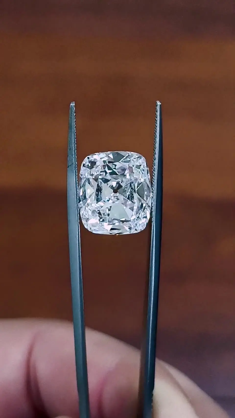 The 7.51 ct D IF diamond held in tweezers near fingertips.