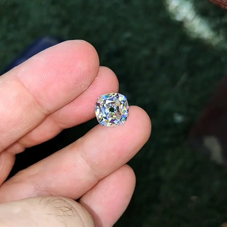 An 8.01 ct old mine cushion held between fingers outdoors.