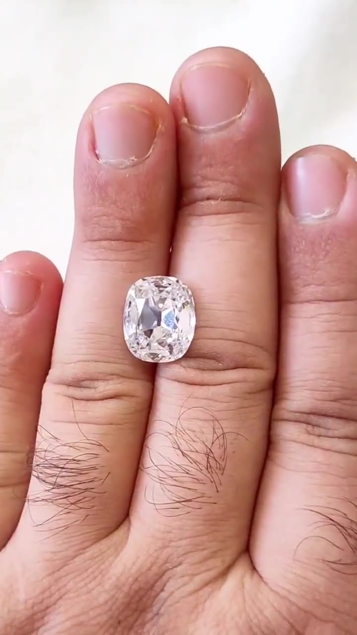 The 9.04 Ct. F IF Old Mine Cushion resting loose on a finger, photographed face-up for scale
